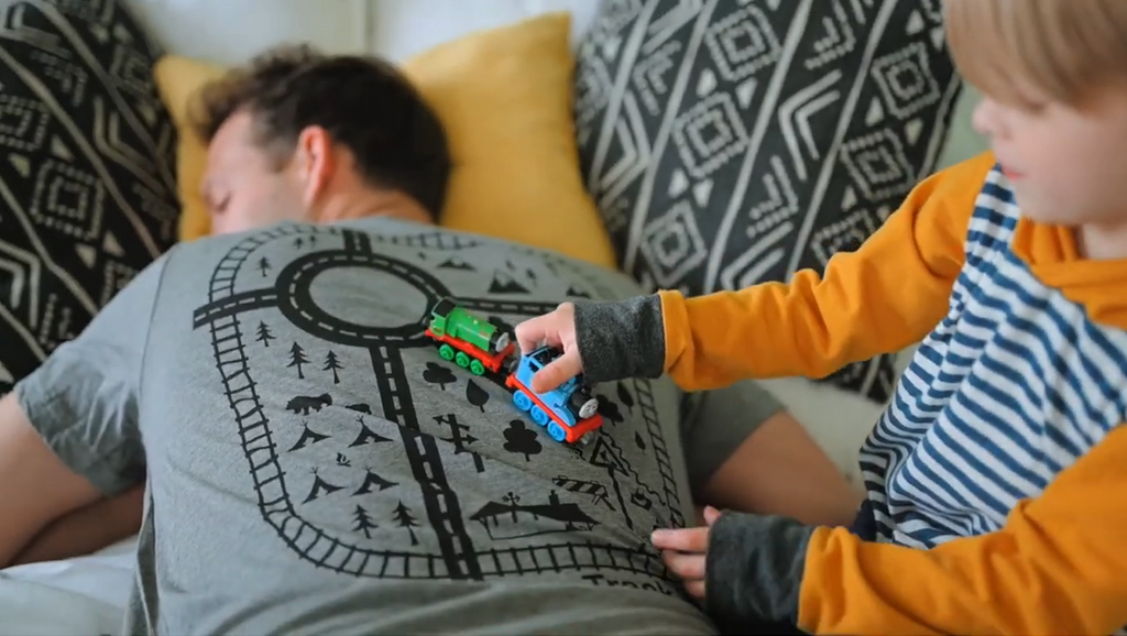 Kid playing trains on his dads back, The dad is wearing a t-shirt with tracks on the back