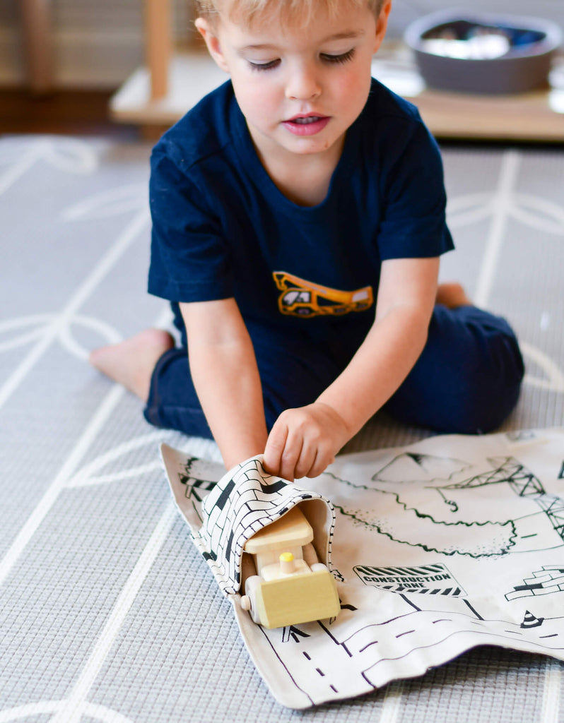 boy playing with wooden digger on a construction play mat